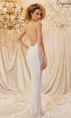 A woman in the Long Prom Dress 30124 by Chandalier, featuring sparkling sequins, lace details, and an open back, stands before draped fabric and chandeliers, glancing over her shoulder.