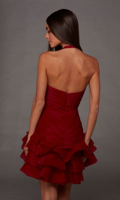 A woman poses with her back to the camera, wearing the Alyce 30127 sleeveless halter-neck layered red crinkle organza short homecoming dress against a plain gray background.