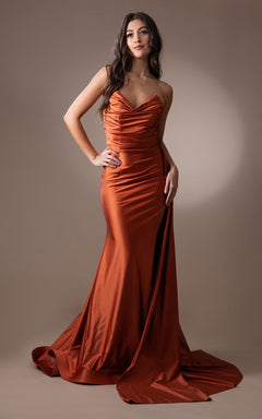 A woman models the Strapless Long Formal Prom Dress with Drape 3013, a rust-colored satin gown with a slight train, exuding timeless elegance in front of a neutral backdrop.