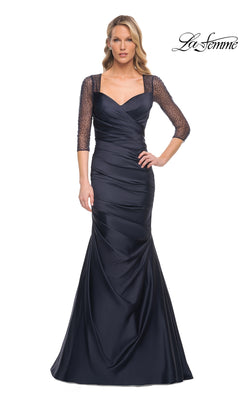 A woman wearing a Long Formal Dress: La Femme 30138, a floor-length navy satin gown with a sweetheart neckline, ruched bodice, and sheer, beaded three-quarter sleeves.