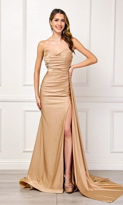 A woman wearing the Strapless Long Formal Prom Dress with Drape 3013 in gold satin, featuring a thigh-high slit, stands indoors against a white paneled wall, smiling at the camera.