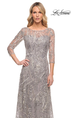 A woman wears the Long Formal Dress: La Femme 30161, a floor-length gray beaded lace dress with three-quarter sleeves and intricate silver sequin embroidery.