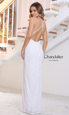 A woman wearing the Chandalier 30179 long prom dress with thin straps and an open back, standing indoors near a staircase.