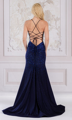 A woman with long blonde hair wears the Open-Back Sparkly Long Beaded Prom Dress 3018, featuring a floor-length silhouette and lace-up open back, standing before a decorative wall.