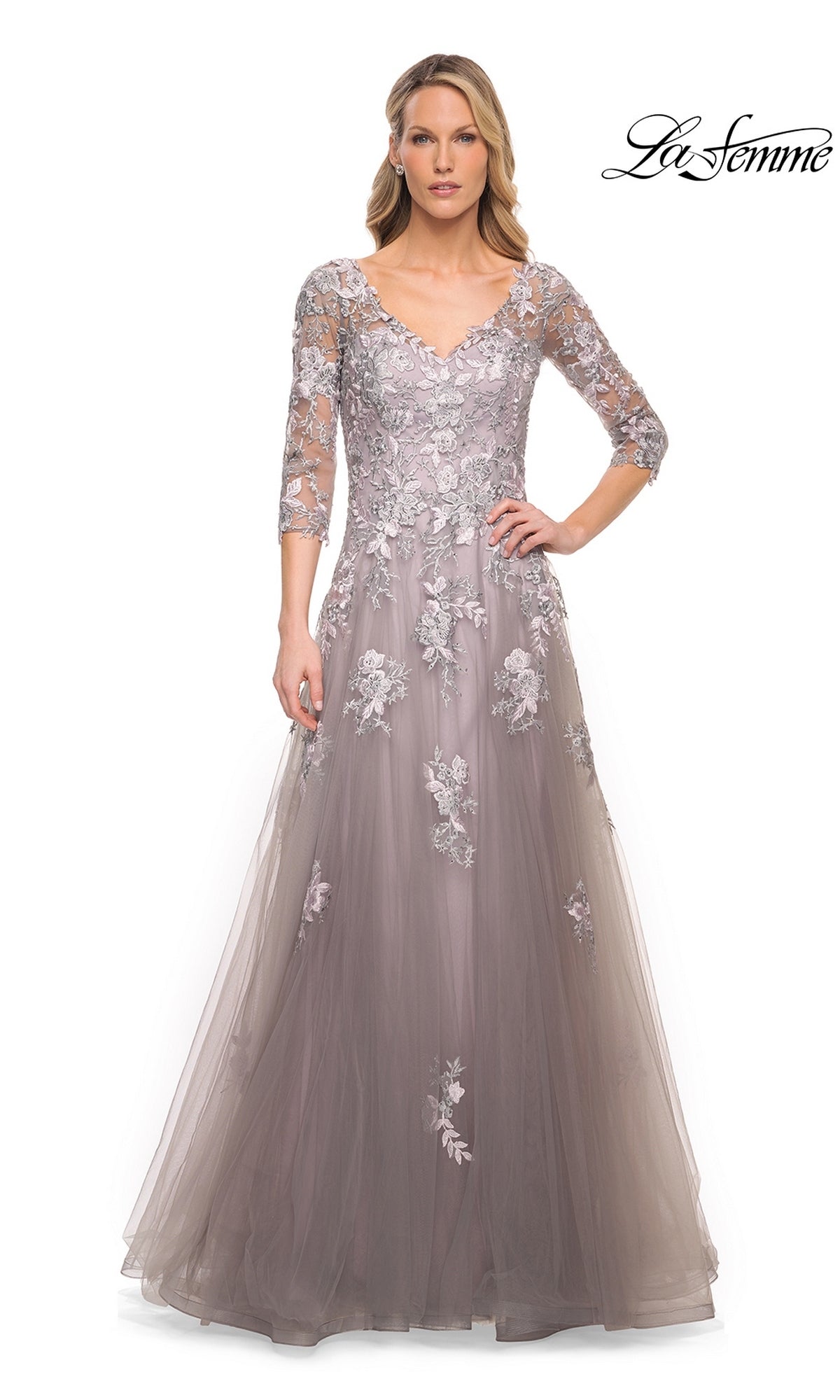 A woman models the Long Formal Dress: La Femme 30229, a silver and pink floor-length gown featuring a V-neckline, three-quarter length sleeves, and intricate floral lace appliques.