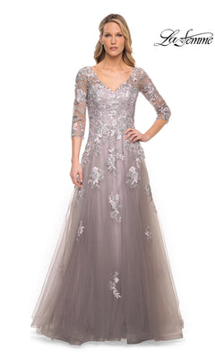 A woman models the Long Formal Dress: La Femme 30229, a silver and pink floor-length gown featuring a V-neckline, three-quarter length sleeves, and intricate floral lace appliques.