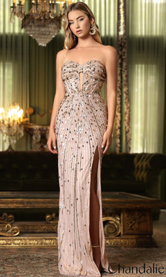 A woman in the gold Long Prom Dress: Chandalier 30237, featuring a strapless sequin bodice and thigh-high slit, stands elegantly in a chandelier-lit room, her gown shimmering under the soft glow.