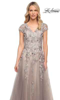 A woman wears a La Femme 30239 silver formal tulle A-line gown with a V-neckline, cap sleeves, and gray floral embroidery with sequins.