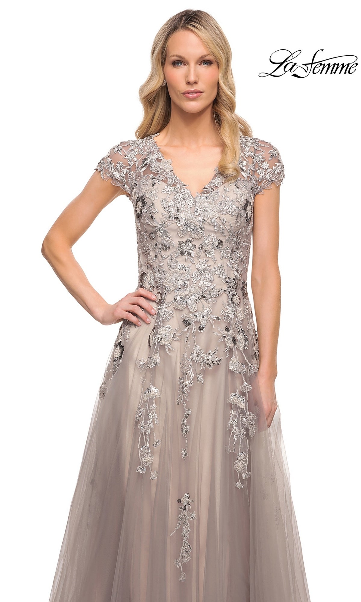 A woman wearing a La Femme 30239 long formal dress with a silver V-neckline, cap sleeves, and floral embroidery over a light taupe tulle A-line gown.