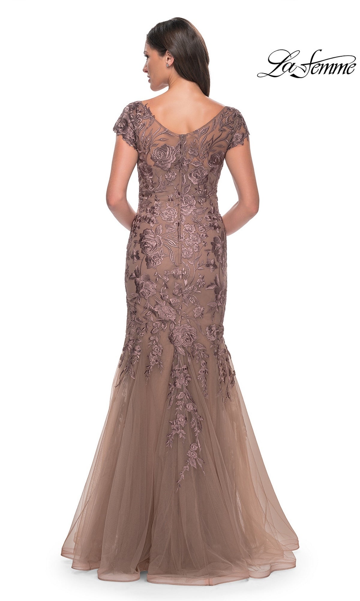 A woman wearing the Long Formal Dress: La Femme 30269, a taupe, floor-length mermaid silhouette gown with short sleeves, a sheer V-neckline, and floral embroidery over a tulle skirt.