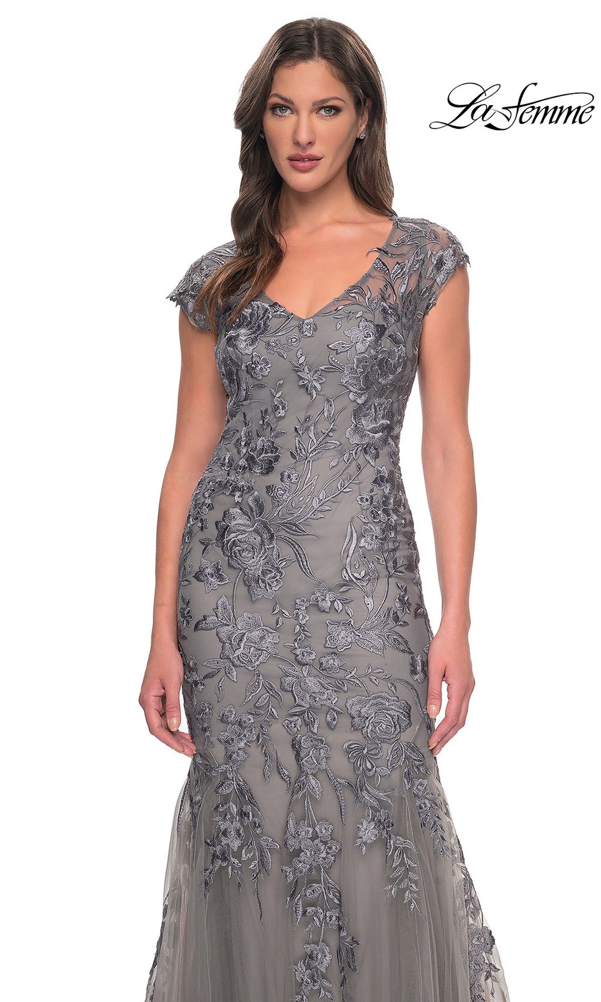A woman wearing a grey, V-neck, cap-sleeve La Femme 30269 long lace formal dress with silver floral embroidery and a flared skirt.
