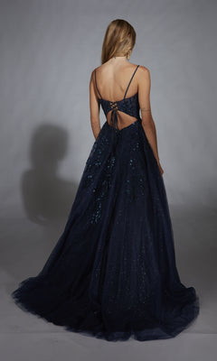 A woman faces away from the camera, wearing the Aerie Couture 302 long prom dress in navy blue glitter tulle with thin straps, a lace-up back, and sparkling sequined accents.