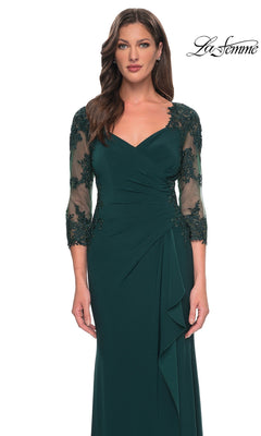 Woman wearing Long Formal Dress: La Femme 30384—an emerald green jersey gown with sheer lace sleeves, floral detail, and a sweetheart neckline. “La Femme” logo in the corner.