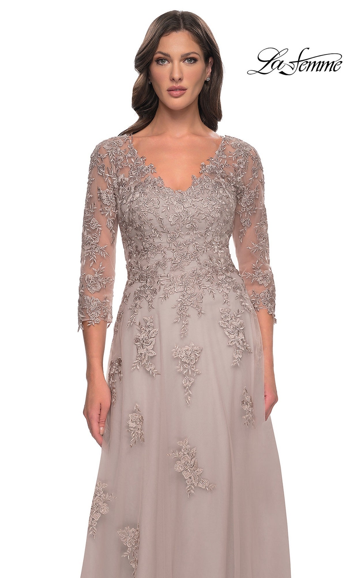 A woman wears a long, light mauve A-line Long Formal Dress: La Femme 30398, featuring a V-neckline, three-quarter length sleeves, and floral lace embroidery over the bodice and upper skirt.