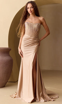 A woman in the Amelia Couture 3042 Beaded-Bodice Long Prom Dress stands indoors by a large vase and arched alcove, her champagne gown with a ruched waist and high slit exuding timeless elegance.