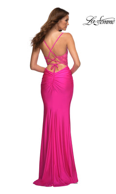 A woman is seen from the back wearing the La Femme V-Neck Neon Pink Long Prom Dress 30606, featuring a floor-length design with a ruched back and crisscross lace-up straps.