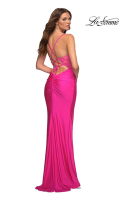 A woman in the La Femme V-Neck Neon Pink Long Prom Dress 30606, featuring ruched back, lace-up straps, and open back, stands looking over her shoulder. The "La Femme" logo appears in the top right corner.