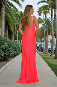 Woman modeling the back of a bright pink dress standing on a sidewalk with palm trees in the background