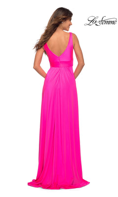 A woman stands facing away in the La Femme Neon Pink Long A-Line Prom Dress 30669, a floor-length sleeveless gown with a deep V-back. The "La Femme" logo appears in the top right corner.