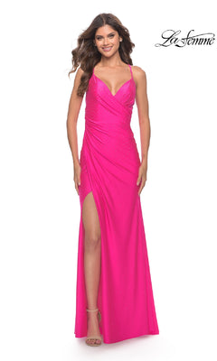Woman models the La Femme 30683 long neon pink prom dress featuring a ruched bodice, thin straps, thigh-high slit, lace-up open back, and subtle embellishments against a white background.