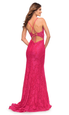 Woman modeling the La Femme 30690 hot pink lace prom dress, featuring a floor-length design, open back with thin crisscross straps, and bow detail, set against a white background.