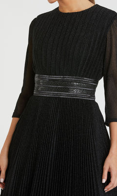 A woman wears the Mac Duggal 30700 Long Glitter A-Line Formal Dress in black, featuring pleats, three-quarter sleeves, and a shiny textured waistband. The upper part of her face is not visible.