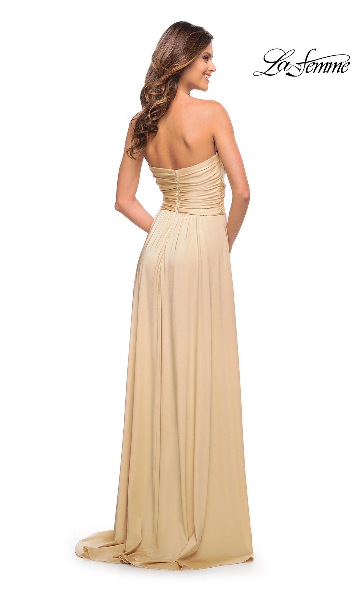 A woman in the Long Prom Dress: La Femme 30700 stands facing away, highlighting the ruched back detail and elegant floor-length silhouette.