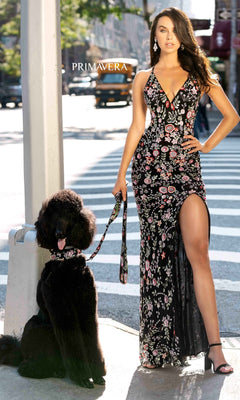 A woman wearing a Beaded Floral Print Long Primavera Prom Dress stands on a city street, holding the leash of a large black poodle with a matching collar and leash.