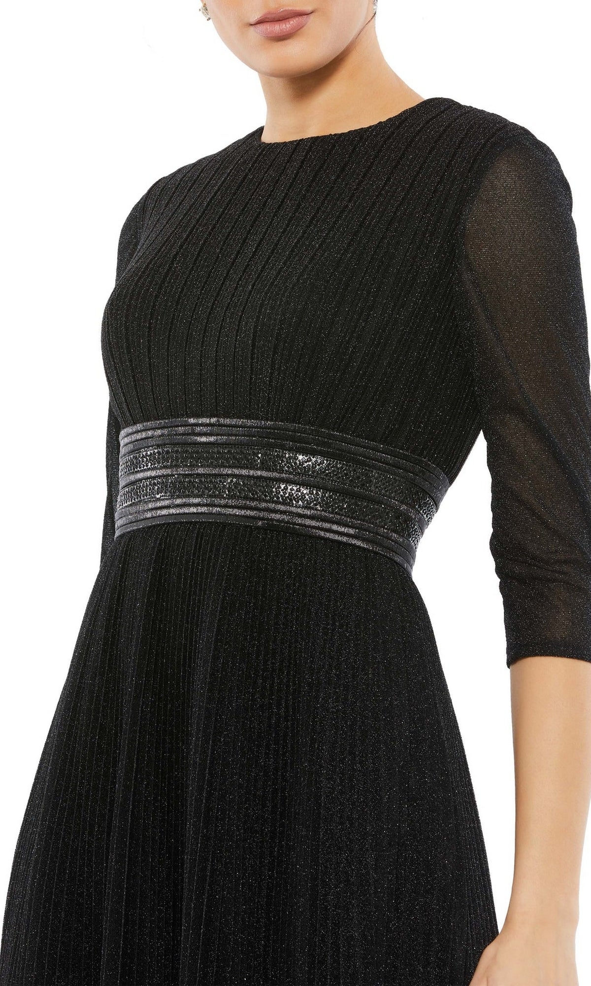 A woman in the Mac Duggal 30750 tea-length wedding guest dress, featuring black textured fabric, sheer three-quarter sleeves, and a shiny metallic waist belt—a chic choice for any celebration.