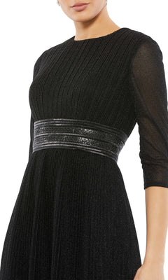 A woman in the Mac Duggal 30750 tea-length wedding guest dress, featuring black textured fabric, sheer three-quarter sleeves, and a shiny metallic waist belt—a chic choice for any celebration.