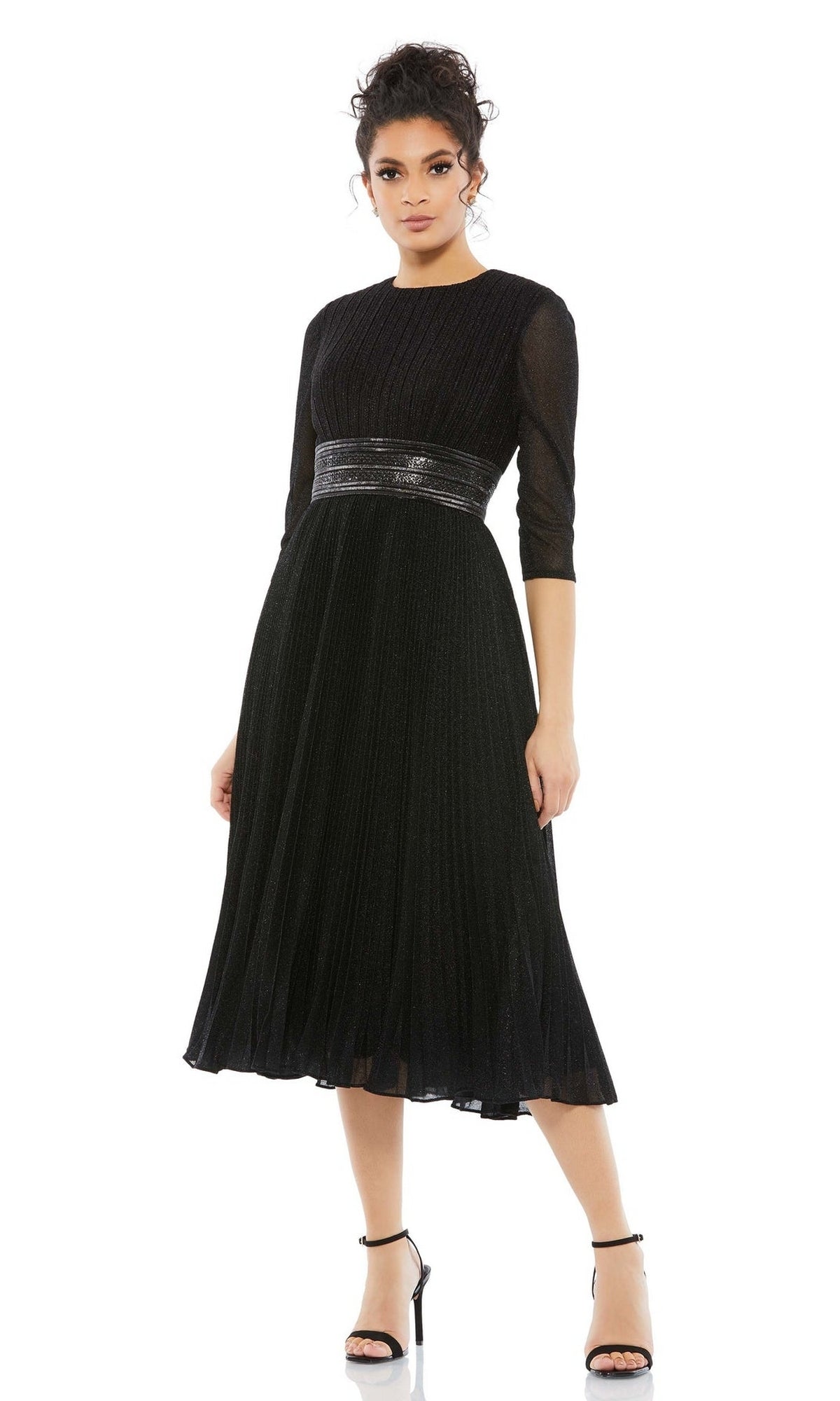 A woman wears the Mac Duggal 30750 tea-length wedding guest dress in black with pleats, three-quarter sleeves, and a metallic belt, paired with black high-heeled sandals.