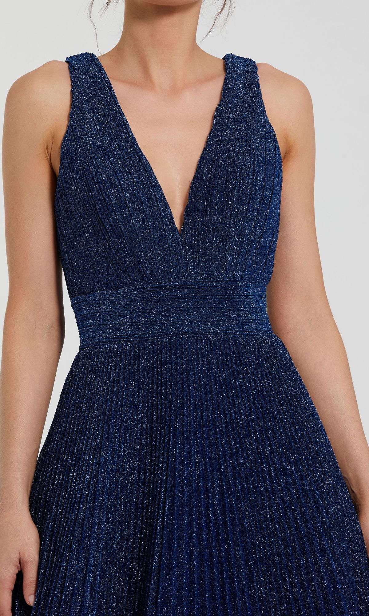 A person wearing the Mac Duggal 30773 long pleated A-line prom dress, featuring a sleeveless deep V-neck design in dark blue with a fitted waistband.