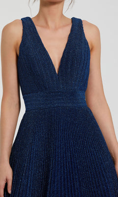 A person wearing the Mac Duggal 30773 long pleated A-line prom dress, featuring a sleeveless deep V-neck design in dark blue with a fitted waistband.