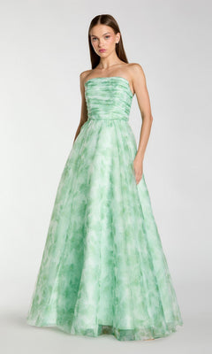 A woman stands facing forward, one hand in her pocket, wearing the Mac Duggal 30783 long formal dress—a strapless green evening gown with a ruched bodice and subtle leaf pattern.