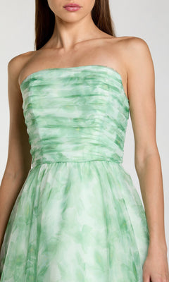 A woman wears the Mac Duggal 30783, a long formal dress with a strapless ruched bodice and light green floral pattern, shown from shoulders to knees.