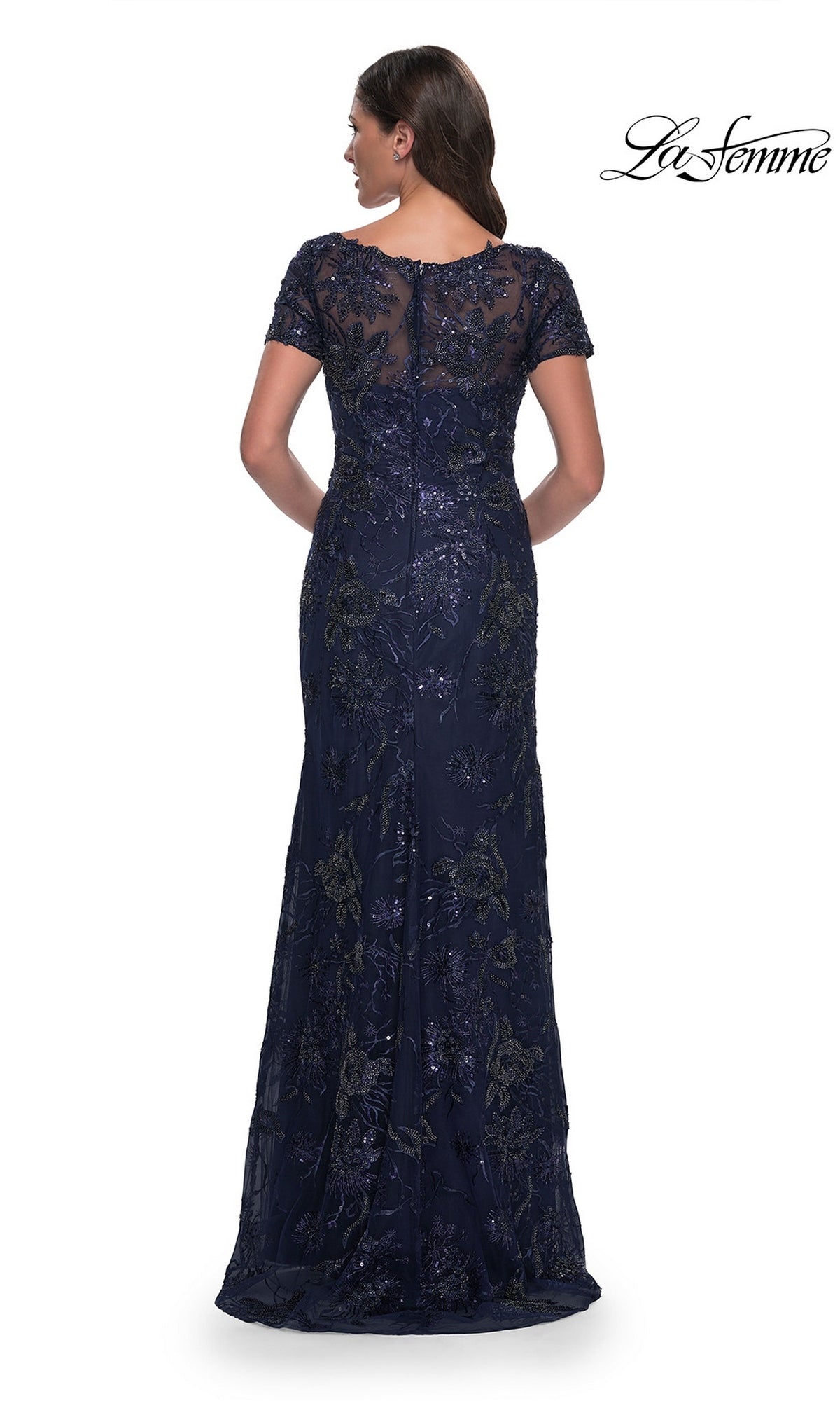 Back view of a woman in a Long Formal Dress: La Femme 30798, a navy blue v-neck gown with short sleeves, a sheer neckline, and intricate sequin floral embroidery.