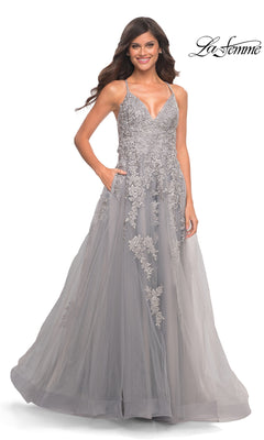 A woman wears a sleeveless, floor-length gray La Femme 30810 prom dress with a V-neckline, embroidered floral appliqués on the bodice, and a full tulle skirt with pockets.