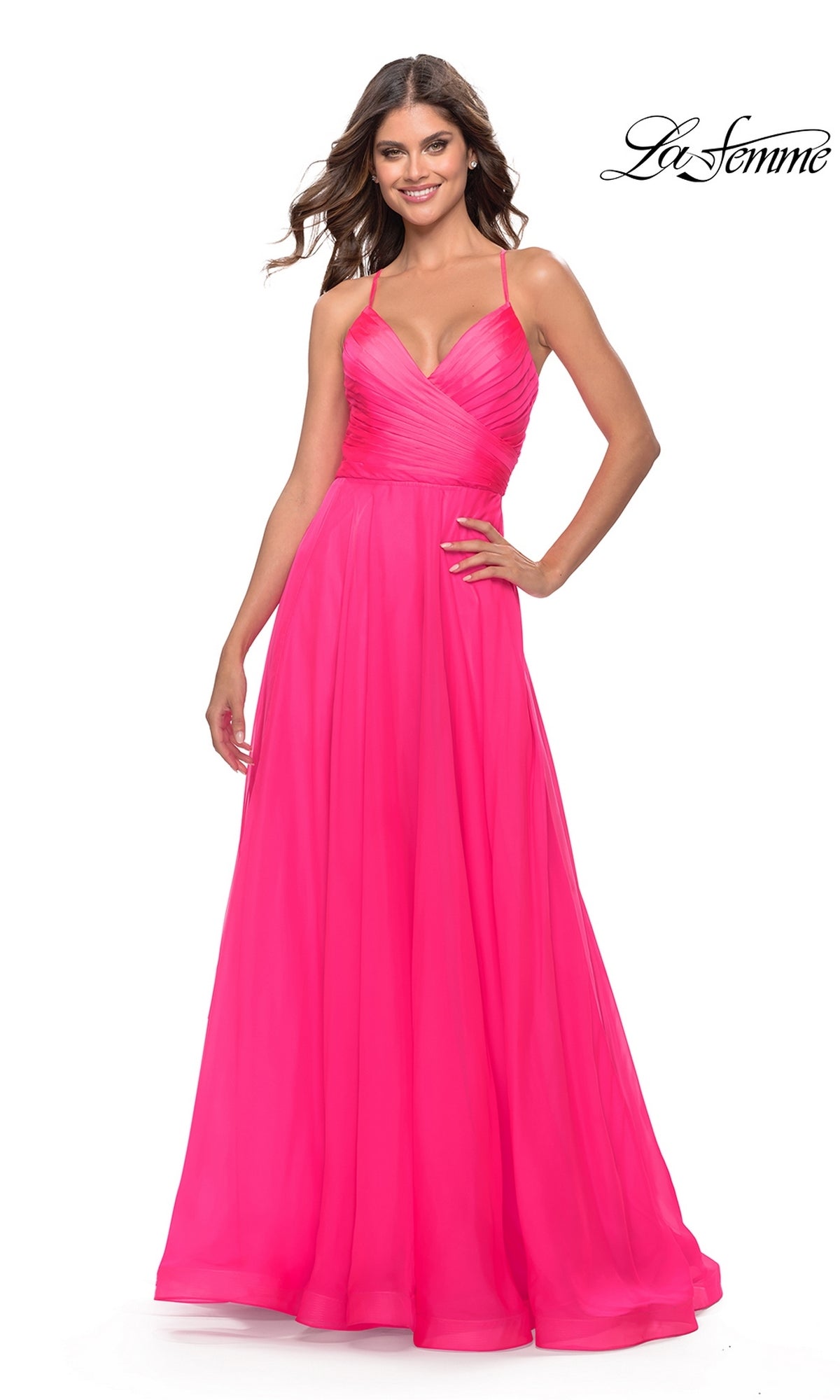 A woman smiles against a white background wearing the La Femme V-Neck Long Tulle Prom Ball Gown 30840, a bright pink, floor-length dress with spaghetti straps and a fitted bodice. The 
