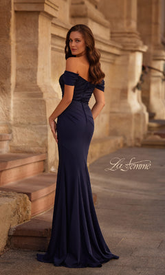 A woman stands outdoors on stone steps in the Off-the-Shoulder Long Formal Dress: La Femme 30846, a fitted mermaid gown with a flowing skirt that creates an elegant silhouette as she looks over her shoulder.