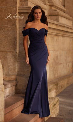 A woman stands on stone steps before a textured wall, wearing the Off-the-Shoulder Long Formal Dress: La Femme 30846—a floor-length navy gown that elegantly drapes for a striking silhouette.