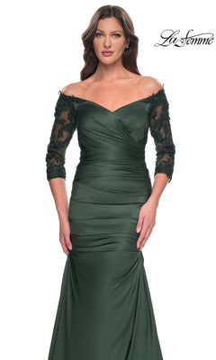 A woman wears the Long Formal Dress: La Femme 30853, a dark green, off-the-shoulder gown with three-quarter length lace sleeves, a ruched bodice, and a trumpet skirt.