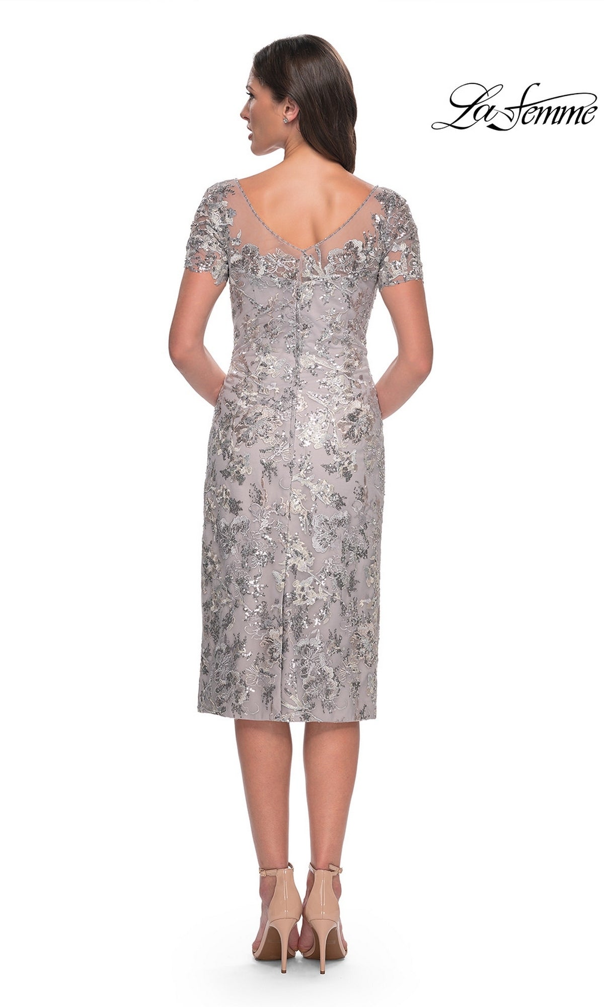 Back view of a silver, metallic embroidered Knee Length Wedding Guest Dress: La Femme 30854, featuring a sheer neckline, short sleeves, and nude high-heeled pumps.