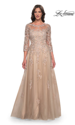 A woman wears a champagne-colored La Femme 30859 floor-length lace applique gown with three-quarter sleeves and floral embroidery over a tulle skirt.