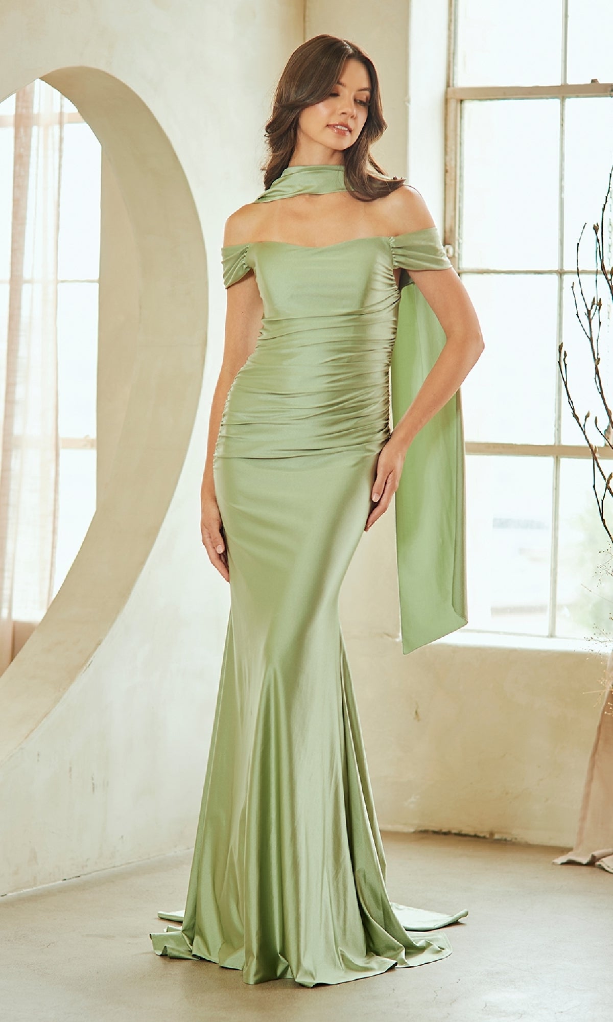 Woman wearing a sage green off-shoulder evening gown in a bright room.