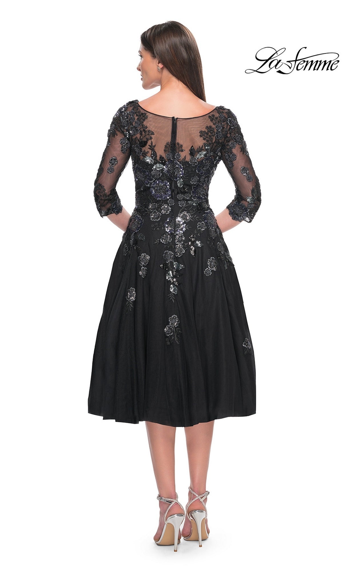 Back view of a woman in the Midi Wedding Guest Dress: La Femme 31017, a black midi dress with a sheer illusion neckline, three-quarter sleeves, and silver sequin lace appliques over an A-line tulle skirt.