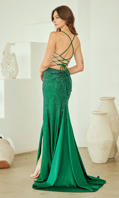 Woman modeling the back of an emerald green evening gown with a backless design in a minimal indoor setting.