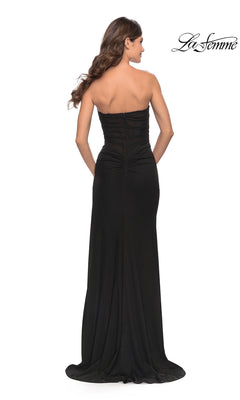A woman with long wavy hair is seen from the back wearing the Sheer-Bodice Strapless Long La Femme Prom Dress in black, with the La Femme logo displayed in the top right corner.