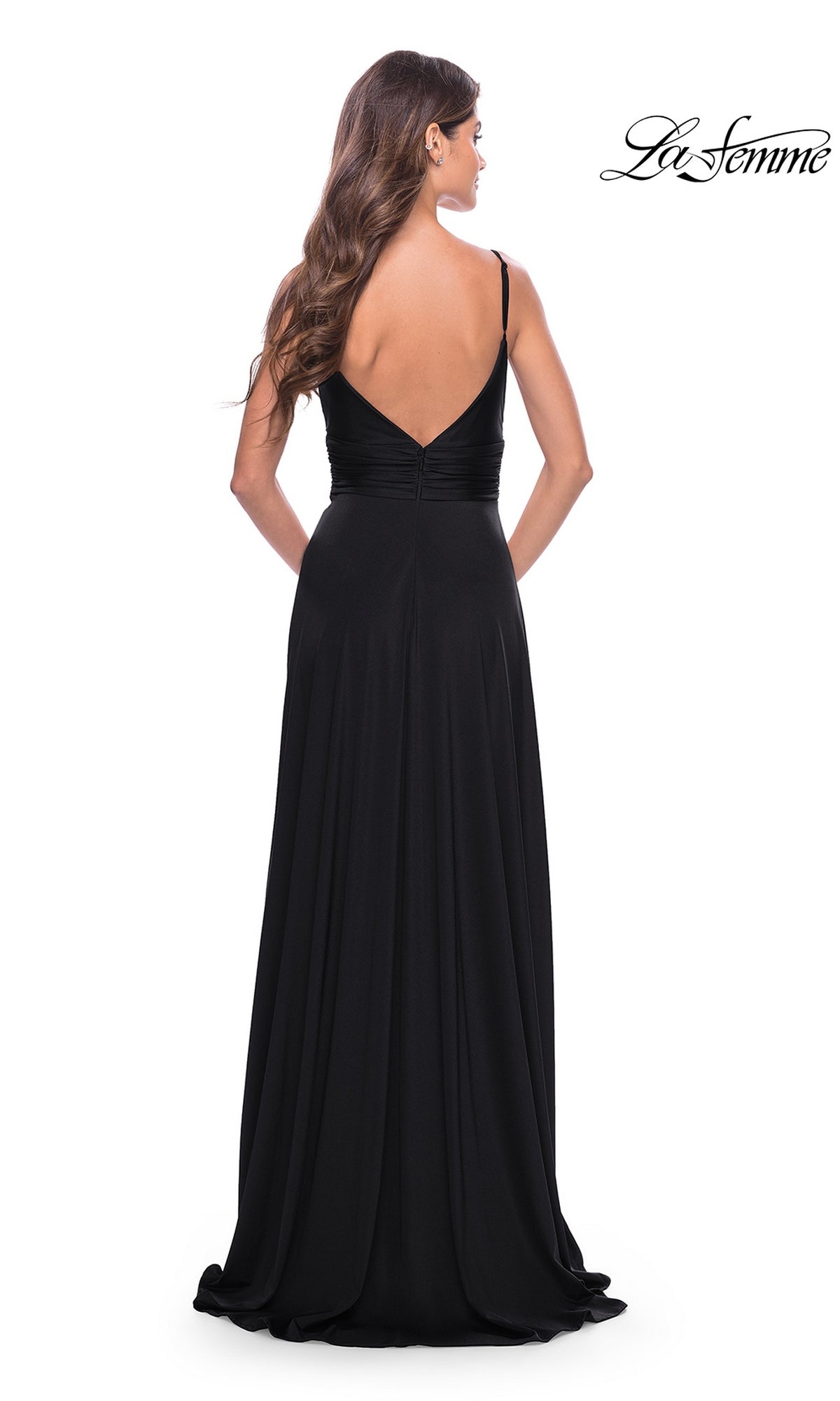 A woman in the La Femme Simple Long A-Line Prom Dress 31090, featuring a deep V-back and ruched bodice, stands facing away from the camera. The 