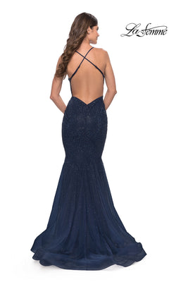 A woman wears the La Femme Long Beaded Mermaid Prom Dress 31119, a navy blue, floor-length gown with thin crisscross straps, sparkling embellishments, and a fitted mermaid silhouette for an elegant look.