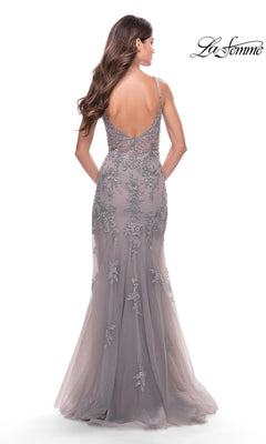 A woman with long brown hair wears the La Femme Long Lace Prom Dress with a sheer bodice, featuring gray floral lace and a low back, as she stands against a white background.